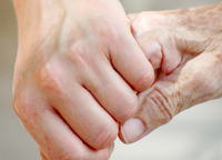 Eine junge Hand hält die Finger der Hand einer älteren Person fest.